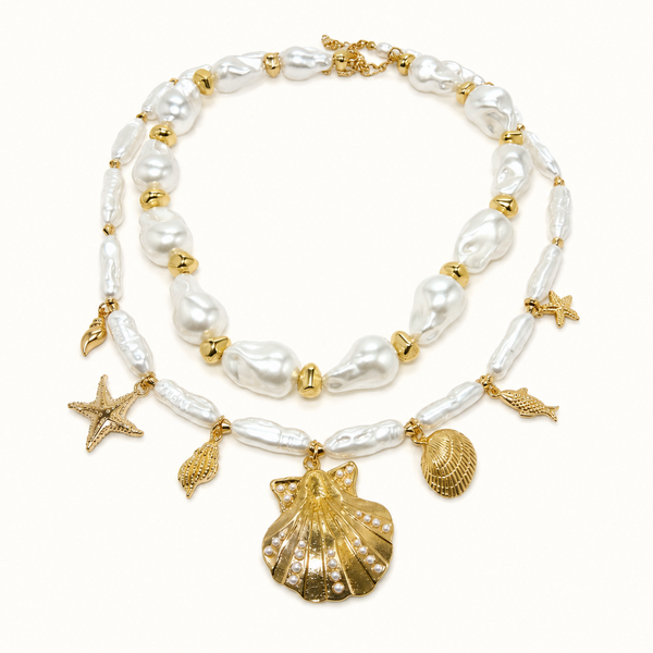A double-strand pearl necklace with gold-tone shell charms, including a large seashell pendant, starfish, and fish-shaped charms, displayed on a clean white background.