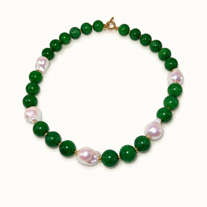 A beaded necklace featuring round green jade-like beads alternating with irregular, lustrous light pink baroque pearls, finished with a gold clasp, shown on a plain off-white background.