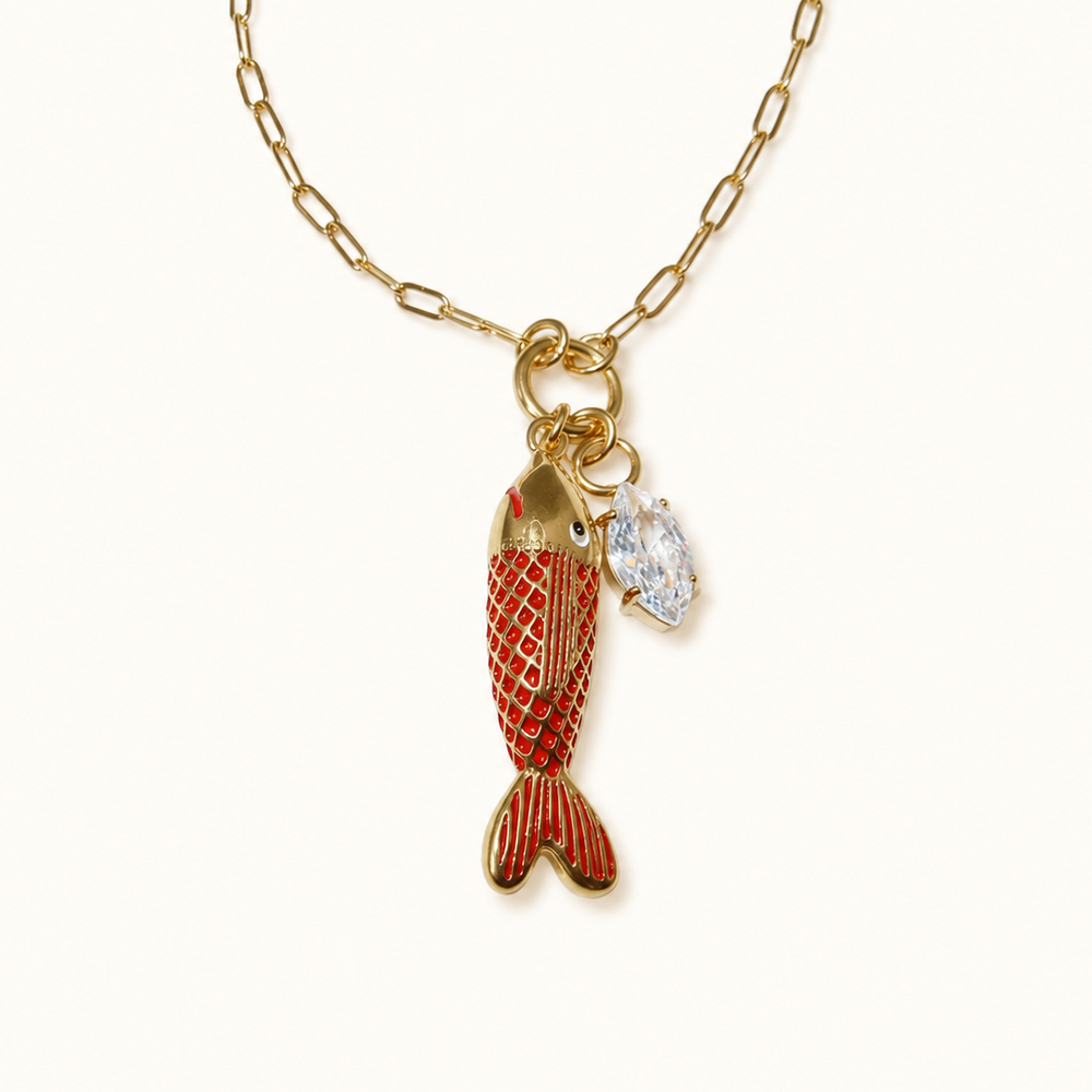 A gold chain necklace featuring a dangling fish charm with red and gold patterned scales and a small clear rhinestone accent, shown on a plain off-white background.