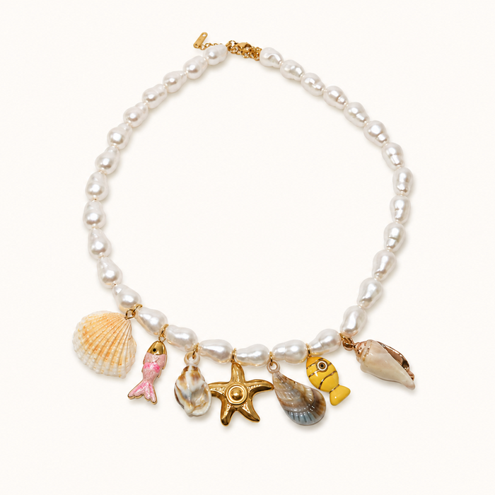 A pearl beaded necklace with gold-tone charms shaped like a seashell, pink mermaid tail, starfish, small shell, and yellow fish, displayed on a clean off-white background.