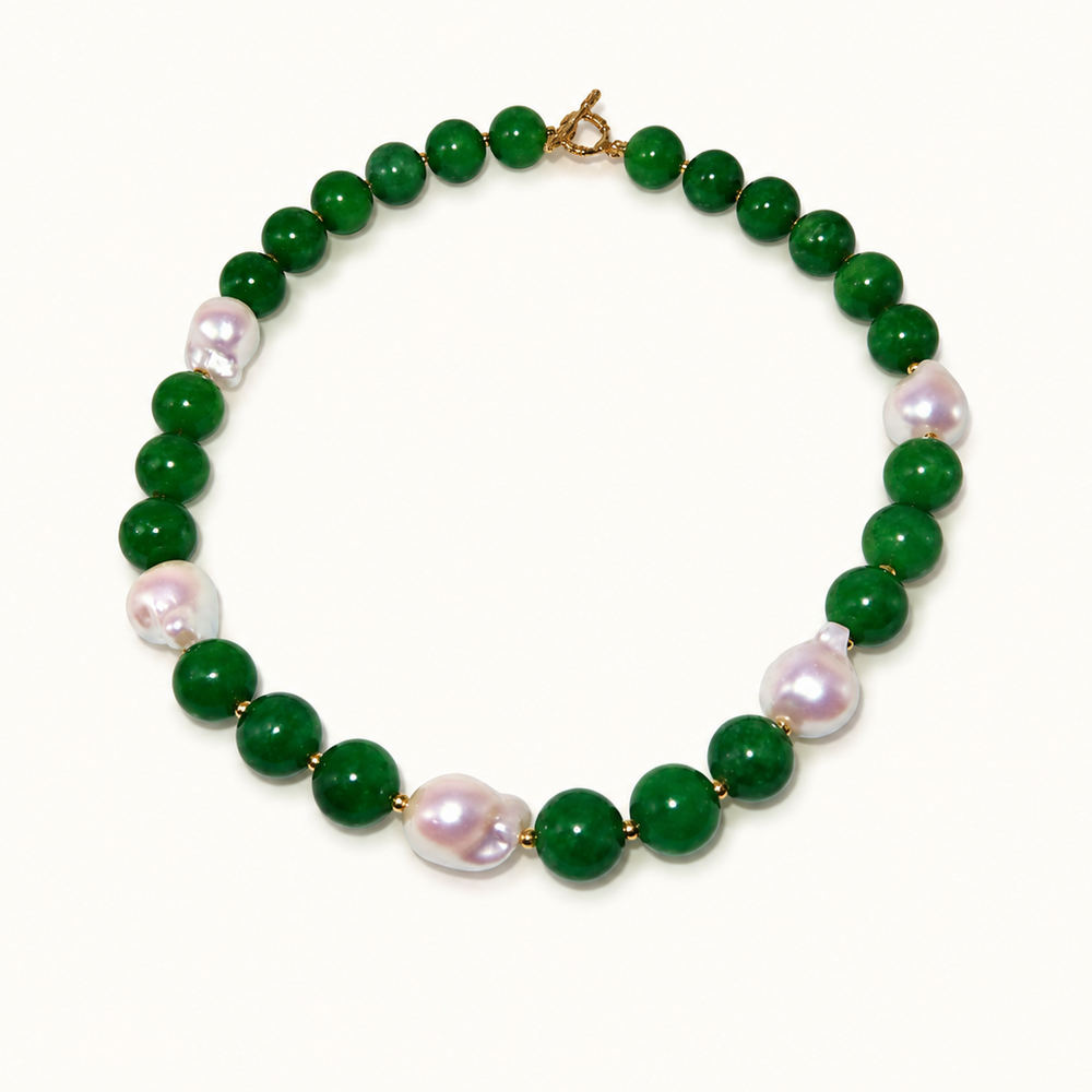 A beaded necklace featuring round green jade-like beads alternating with irregular, lustrous light pink baroque pearls, finished with a gold clasp, shown on a plain off-white background.