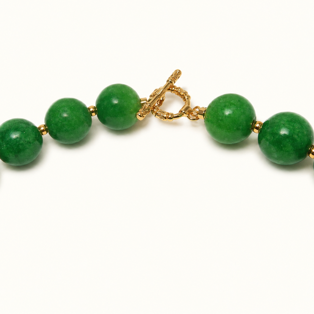 A close-up of a beaded necklace with round green jade-like beads and a gold toggle clasp, shown on a plain white background.
