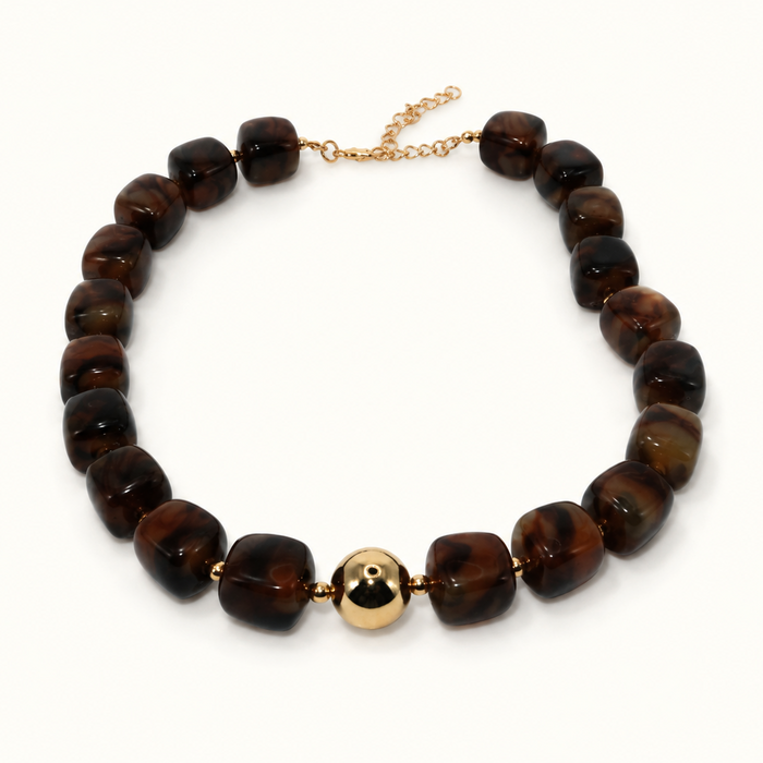 A beaded necklace featuring glossy, rounded dark brown beads with natural tiger's eye patterns, accented by a single polished gold-colored central bead and a gold-tone extender chain clasp, shown on a plain white background.