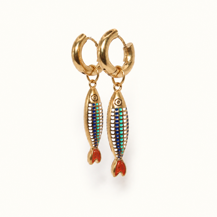 A pair of gold huggie hoop earrings with dangling fish charms. The fish charms feature a textured body with green, blue, and white stripes, and red-orange tails, shown on a clean white background.