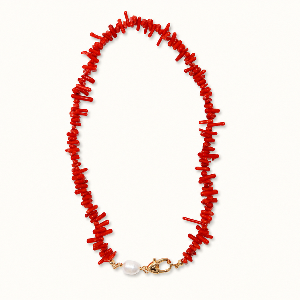 A coral-style necklace made of small bright red fragments, with a gold-tone clasp and a single white pearl accent at the bottom, shown on a plain light background.