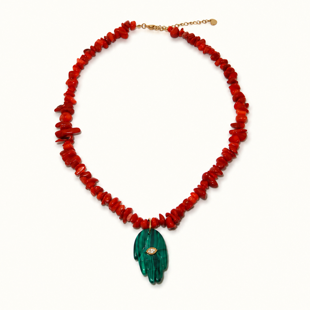 A chunky red beaded necklace with a green hand-shaped pendant featuring a small gold and white stone in the center, displayed on a clean white background.