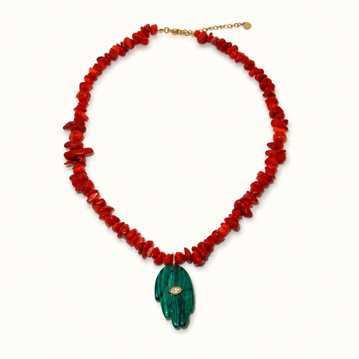 A chunky red beaded necklace with a green hand-shaped pendant featuring a small gold and white stone in the center, displayed on a clean white background.