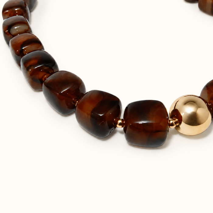 A close-up of a beaded necklace featuring polished dark brown tiger's eye stones and a single shiny gold spacer bead, set against a plain white background.